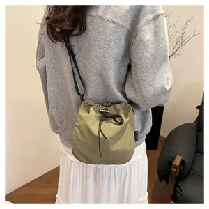 Casual olive green nylon drawstring bucket bag worn as a stylish crossbody bag for women