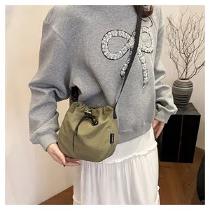 Close-up of lightweight olive green nylon drawstring bucket bag worn as a crossbody