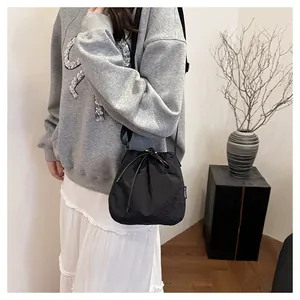 Model wearing a black lightweight nylon drawstring bucket bag as a crossbody.