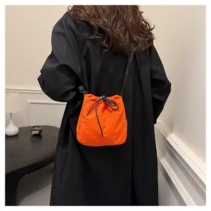 Back view of a vibrant orange nylon drawstring bucket bag worn over a black coat