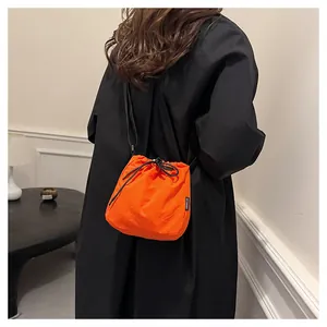 Detailed view of a bright orange nylon drawstring bucket bag worn over a black coat