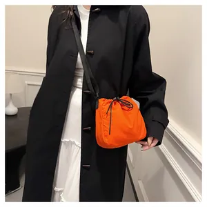 Detail view of vibrant orange nylon drawstring bucket bag worn crossbody with black coat