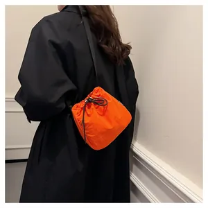 Detail shot of a vibrant orange nylon drawstring bucket bag on a black coat.