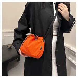 Close-up of a model wearing a vibrant orange nylon drawstring crossbody bucket bag