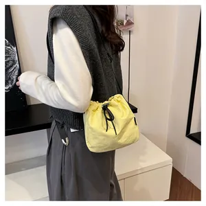 Model wearing a lightweight yellow nylon drawstring bucket bag in a casual indoor setting