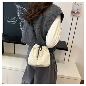 Lifestyle detail of a cream nylon drawstring bucket bag worn as a crossbody bag