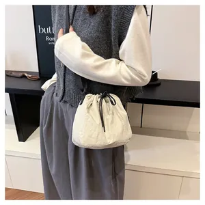 Lifestyle shot of a cream nylon drawstring bucket bag worn by a model in a cafe setting