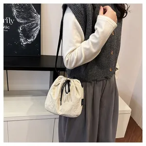 Lifestyle view of a lightweight cream nylon drawstring bucket bag carried by a model