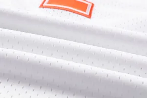 Close-up detail of white breathable mesh basketball jersey fabric with orange embroidery.