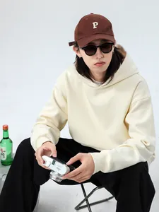 Detail view of a male model wearing an oversized cream hoodie and brown baseball cap