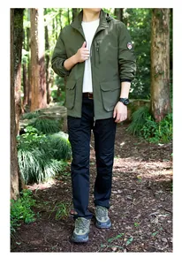 Model wearing an olive green hooded outdoor windbreaker standing on a forest path
