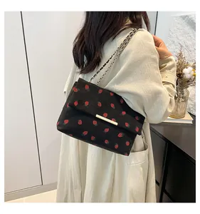 Detail view of a black corduroy shoulder bag with red strawberry pattern worn by a model