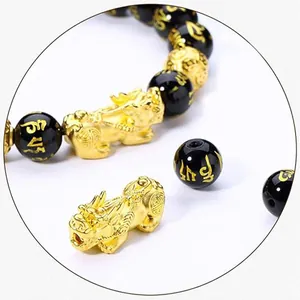 Detailed view of gold PiXiu charm and black obsidian beads with gold mantra engravings.