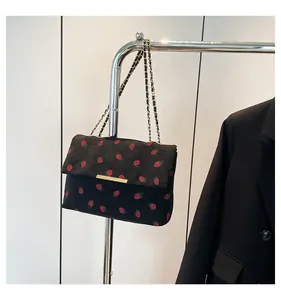 Detailed close-up view of a black corduroy strawberry print handbag hanging on a rack.