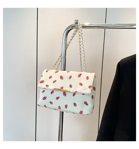 Detailed close-up of a white corduroy shoulder bag featuring a cute red strawberry print pattern