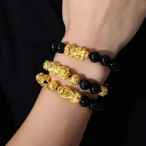 Macro detail showing the texture of golden Pixiu charms on black obsidian bracelets.