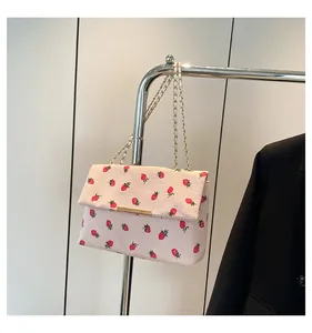 Detail of a pink corduroy shoulder bag with red strawberry prints and gold chain.