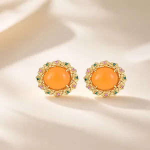 Detalle de elegantes pendientes de botón redondos con cabujón naranja y marco floral.