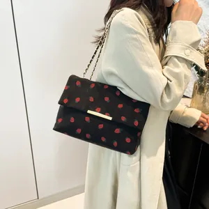 Chic black corduroy shoulder bag with vibrant red strawberry pattern worn by model