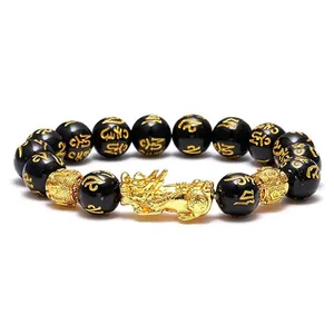 Close-up view of a gold-toned Pixiu charm and black obsidian beads with mantra engraving