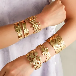 Detailweergave van retro gouden chunky manchetarmbanden met bloem- en veerpatronen