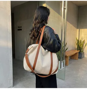 Side detail shot of large canvas tote bag with brown leather straps on model's shoulder.