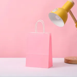 Detailed view of the pink kraft paper gift bag with white handles on a desk