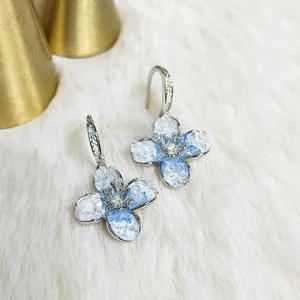 Pendientes de flores azules degradadas con brillantes sobre piel blanca