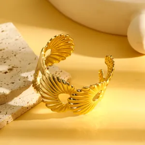 Close-up van een gouden roestvrijstalen armband met ingewikkeld opengewerkt schelpenpatroon.