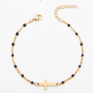 Bracelet en acier titane plaqué or avec perles en émail noir et une breloque croix.