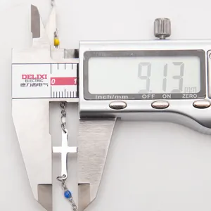 Vue détaillée d'un pendentif croix en acier inoxydable mesuré par un pied à coulisse numérique.