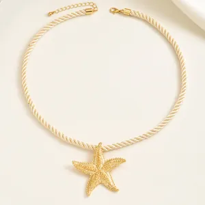 Primo piano di un ciondolo a stella marina dorata su una collana in corda intrecciata.