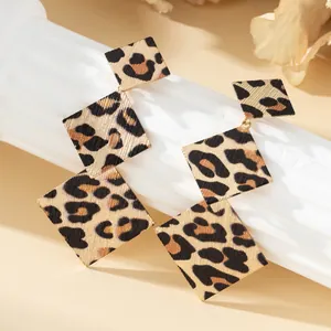 Dettaglio di eleganti orecchini pendenti a triplo quadrato con stampa leopardata su bianco.