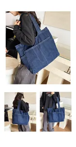Detail of a large capacity blue denim tote bag worn by a model in a stylish room.