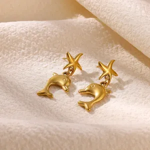 Close-up of golden stainless steel starfish and dolphin drop earrings on soft fabric background