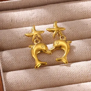 Detailed close-up view of golden starfish and dolphin dangle earrings on a beige linen background