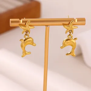 Close-up of golden stainless steel earrings with starfish and dolphin ocean designs
