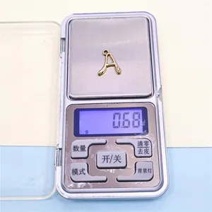 Vista detallada de un colgante de letra A de aleación dorada en una báscula que pesa 0,68g