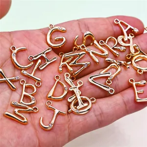 Primer plano de dijes de letras del alfabeto de aleación dorada con pedrería para joyería DIY.