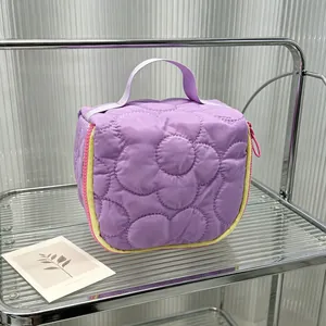 Detail view of a quilted purple floral cosmetic bag with a handle on a glass shelf.