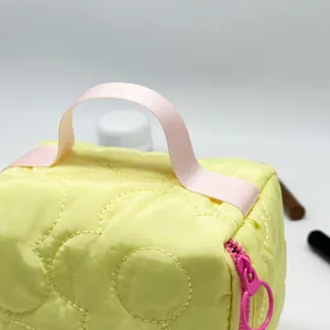Close-up detail of yellow quilted makeup bag showing pink handle and circular zipper pull