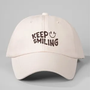 Cream cotton baseball cap featuring a brown 'Keep Smiling' print and smiley face icon