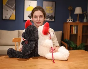 Black and white plush teddy bears with red hearts held by a model for a gift showcase