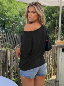 Back view of a woman wearing a loose black one-shoulder T-shirt in an outdoor garden