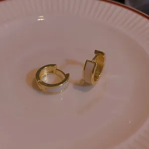 Detailed macro view of gold-tone hoop earrings with white enamel inlay on a porcelain plate