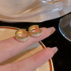 Close-up of small gold hoop earrings with white enamel dripping oil inlay on fingers.