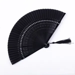 Primer plano de abanico plegable lacado negro con intrincados calados y borla de seda