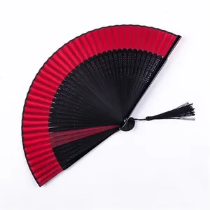 Detalle de un abanico plegable chino clásico en rojo y negro con una borla negra.