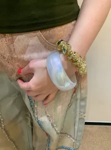 Detail view of chunky iridescent resin bangle and gold chain bracelet on model's wrist