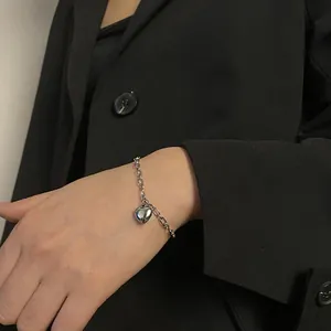 Close-up of a minimalist silver heart pendant bracelet on a wrist against a black blazer